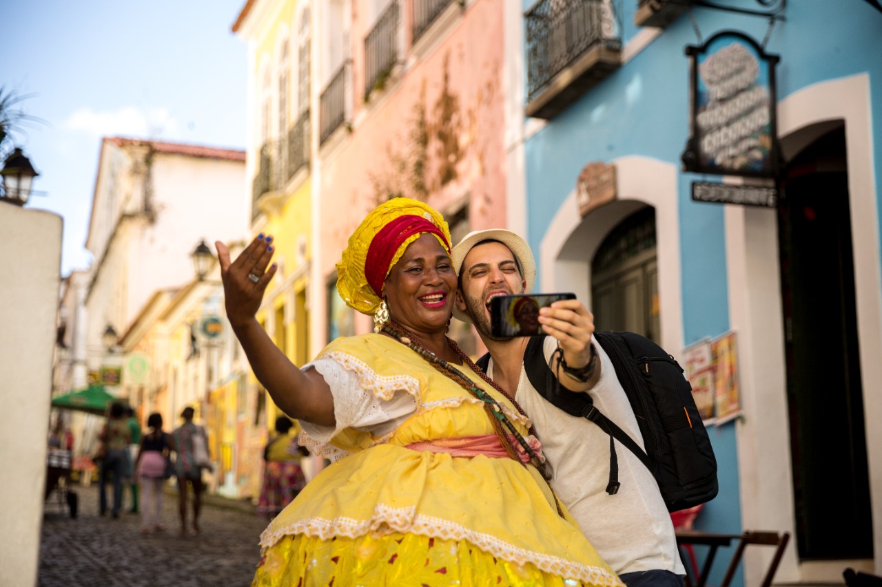 Γυναίκα με κίτρινη στολή ποζάρει με έναν τουρίστα που βγάζει φωτογραφία στην Κούβα