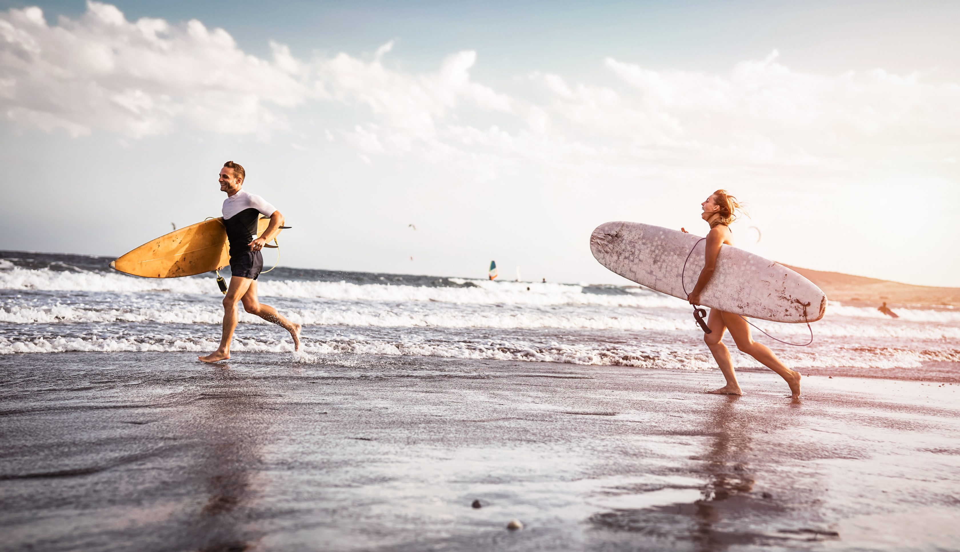 Ένα ζευγάρι από σέρφερ τρέχουν στην παραλία και διασκεδάζουν 